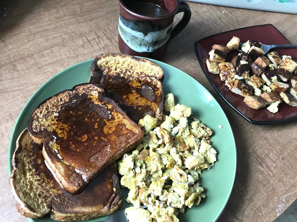 An appetizing plate of wheat bread French toast with scrambled eggs, syrup and coffee, a small plate on the side with cubed French toast for my toddler mixed with scrambled eggs and syrup.