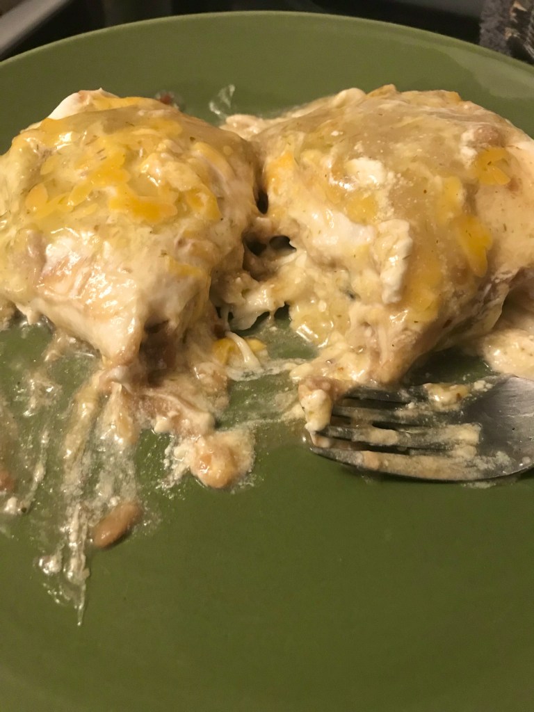 Green sauce chicken enchiladas, with sour cream, refried beans, olives and mozzarella cheese in a flour tortilla and baked.