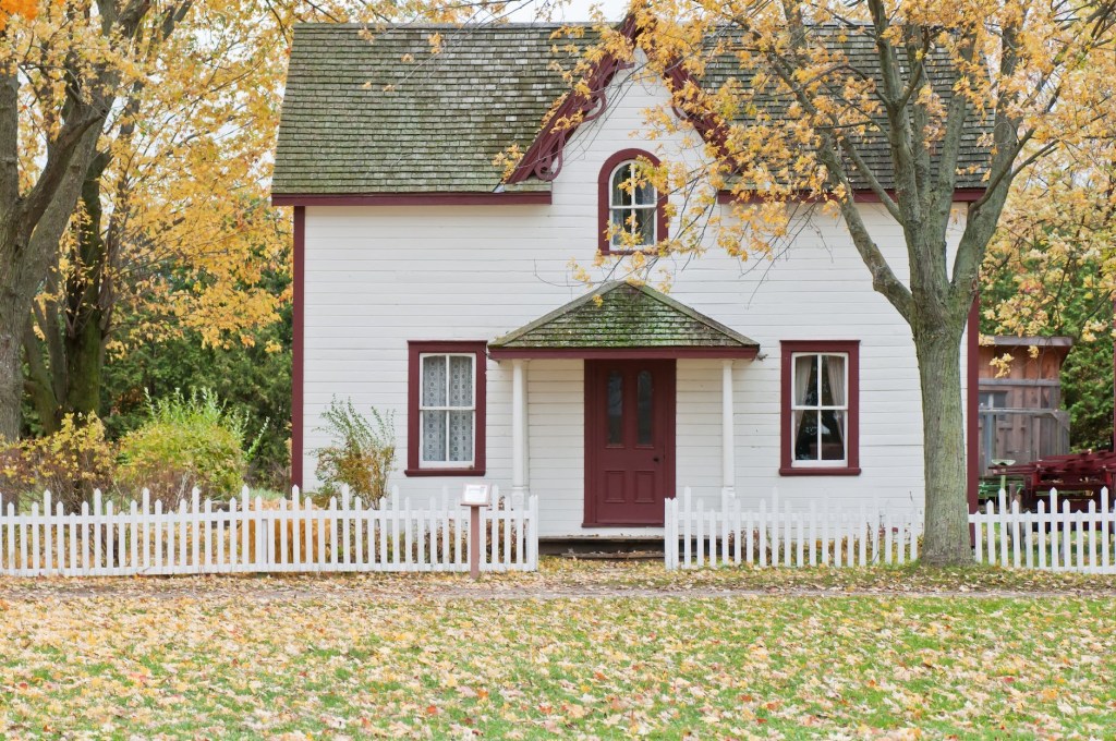 White farm house with red trim surrounded my yellow autumn leaves and trees
