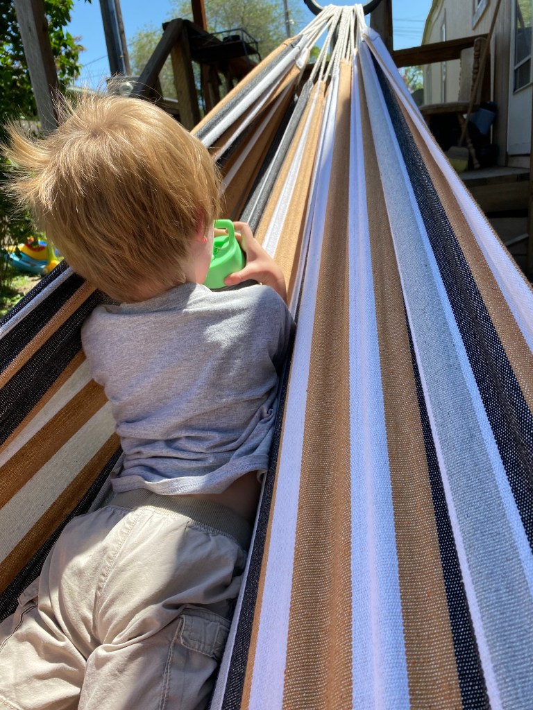 My toddler son laying in our outdoor freestanding hammock in the sun