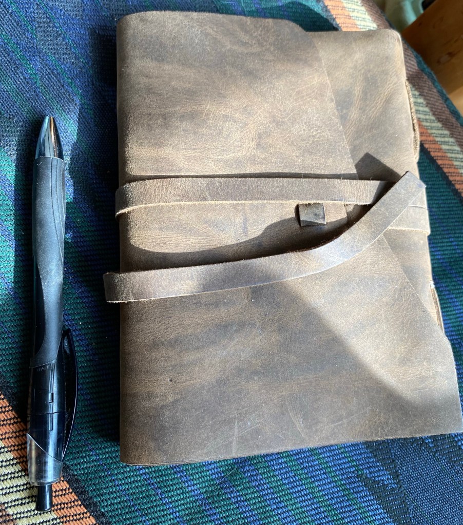 Faded brown leather journal next to a black pen sitting on a western/native patterned cushion.