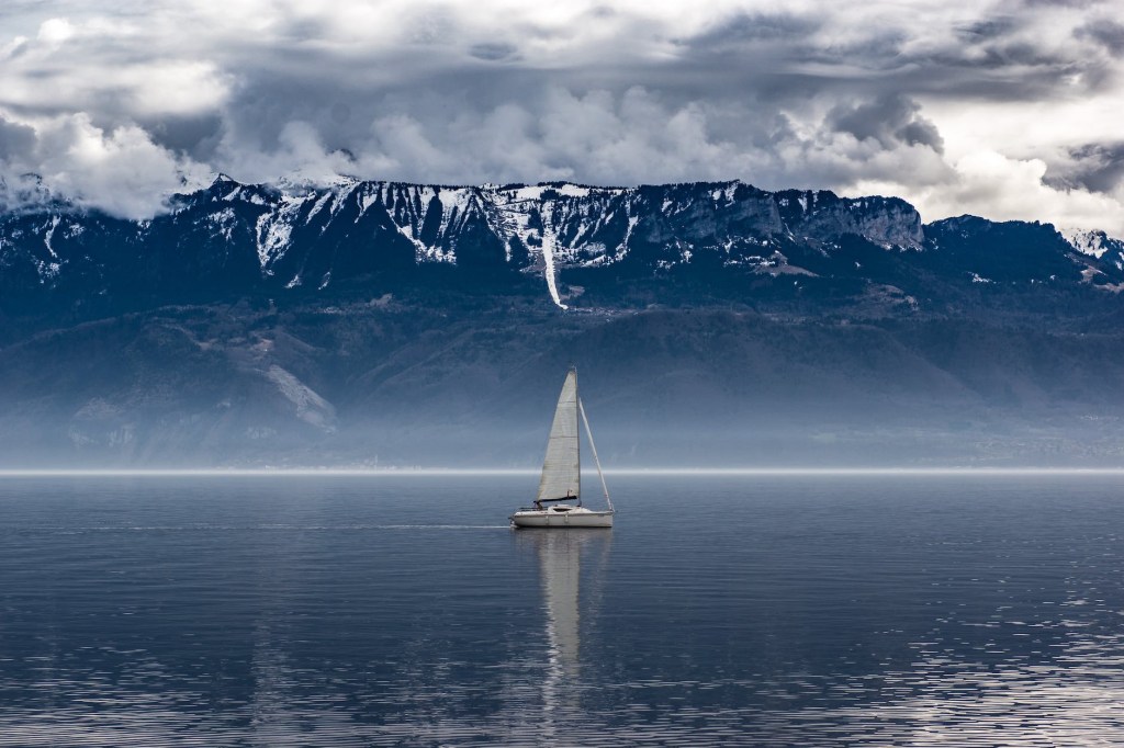 Ship sailing in calm waters, snowy mountain scape behind.