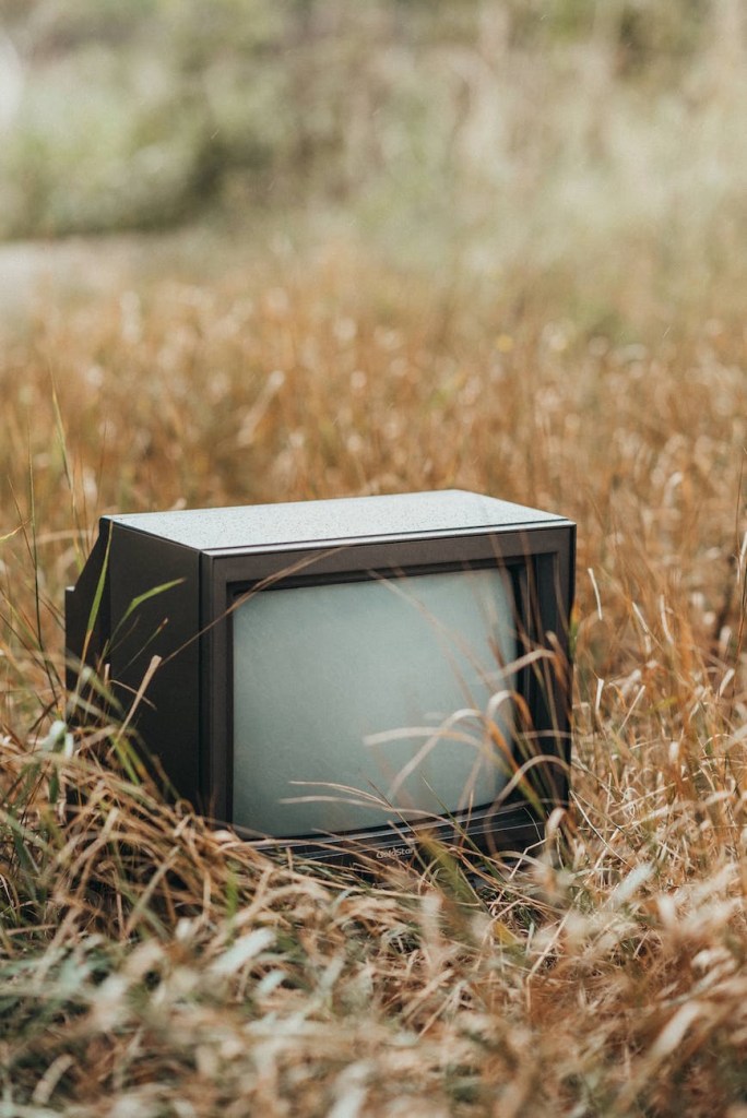 Old box tv sitting in tall yellow grass