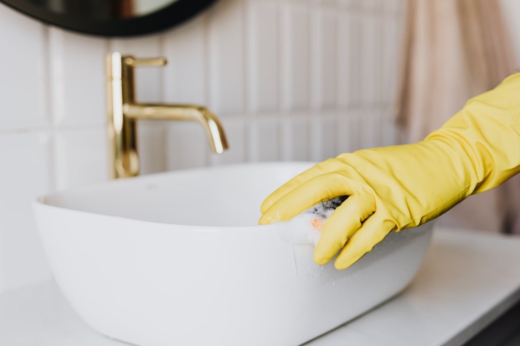Yellow cleaning glove and sponge cleaning a rich beautiful sink