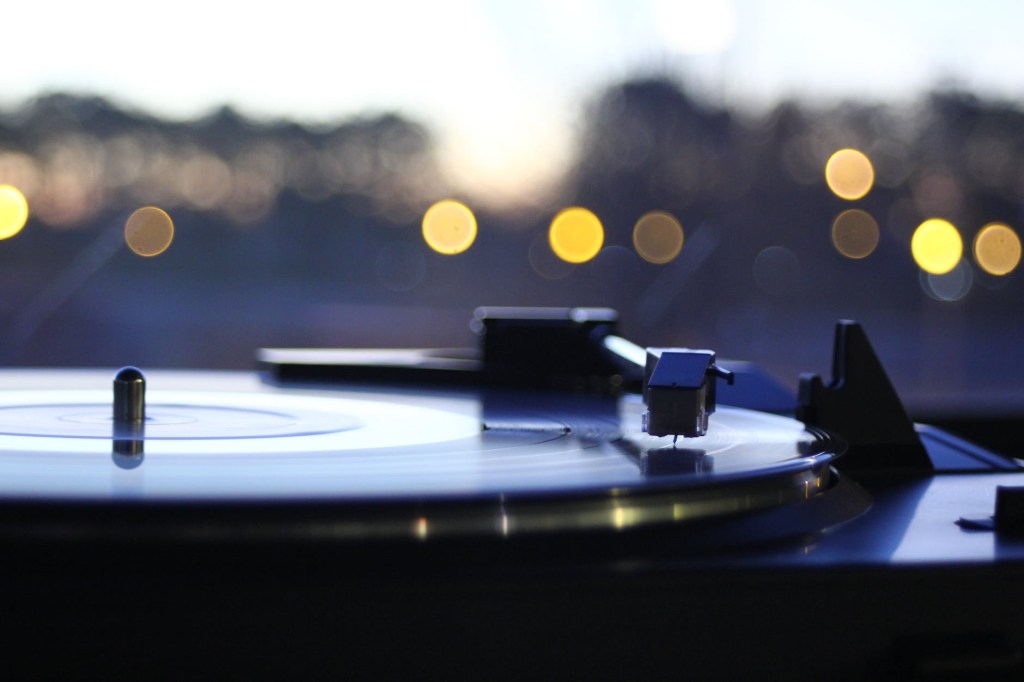 Side view of a record on a record player with the background of blurred lights outdoors at dusk
