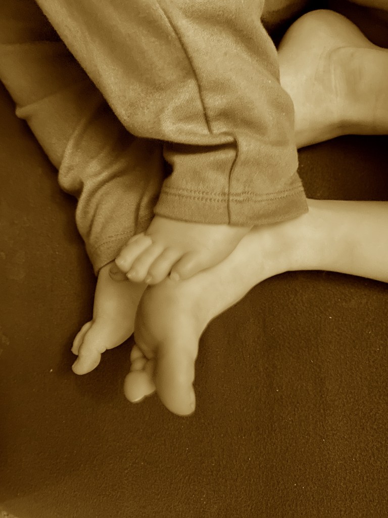Two sets of toddler feet sole to sole, one pair smaller than their sibling’s 